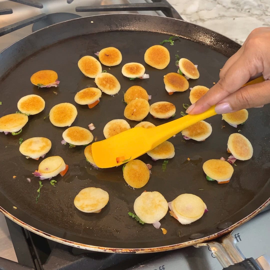 flipping bite sized uttapam to cook top side 