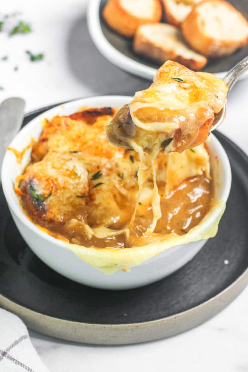 French onion soup in a white bowl with a some soup in a spoon