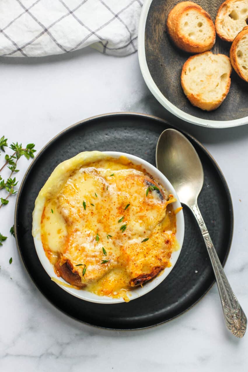 French onion soup in a white bowl with a spoon on the side 