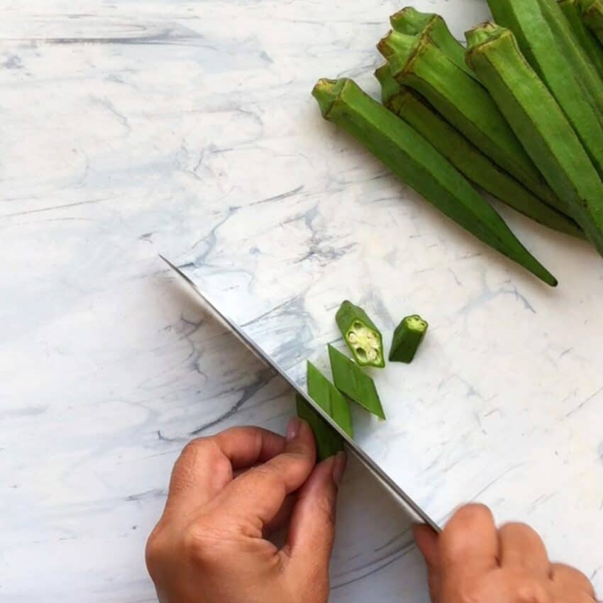 slicing okra on a white cutting board 