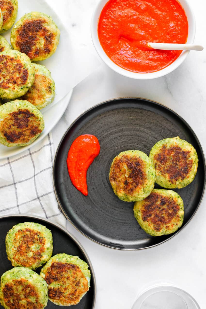 three broccoli and tofu patties on a black plate with red pepper chutney