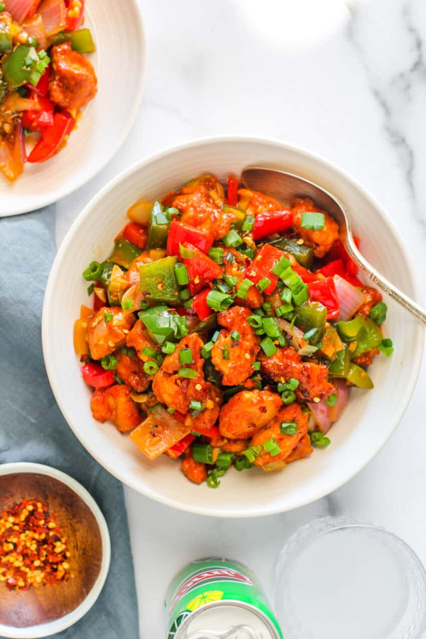 chilli chicken served in a white bowl with a spoon 