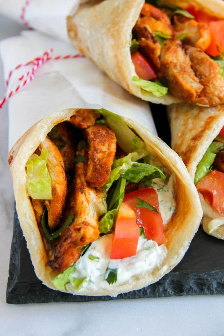 close up photo of chicken shawarma rolls with lettuce, tomatoes and tzatziki