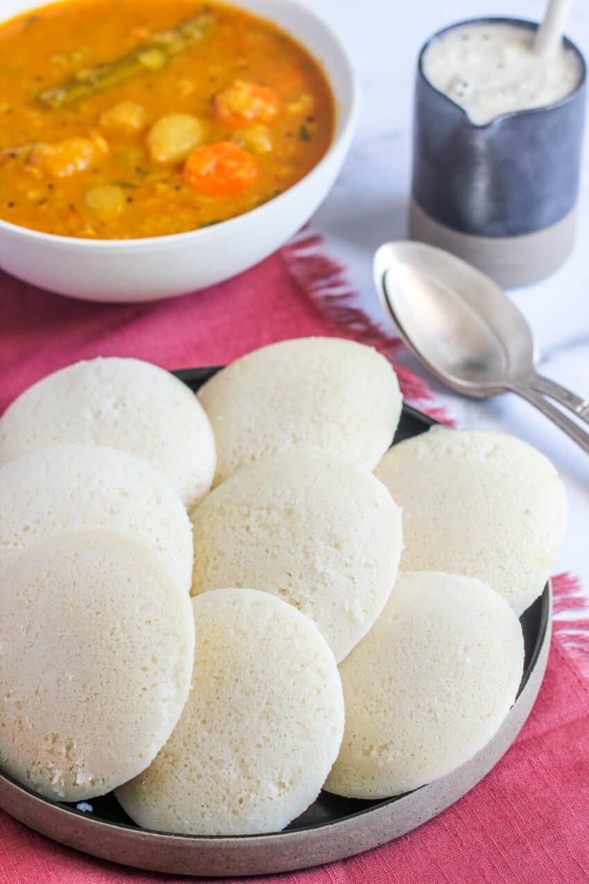 steamed rice cakes next to a bowl of sambar and coconut chutney 