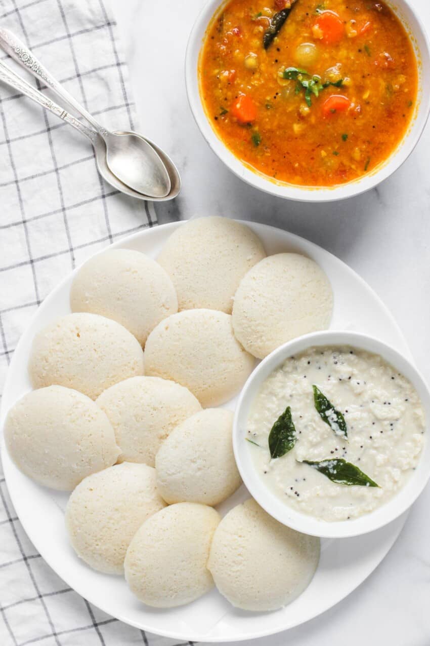 idli in a white platter with coconut chutney in a bowl