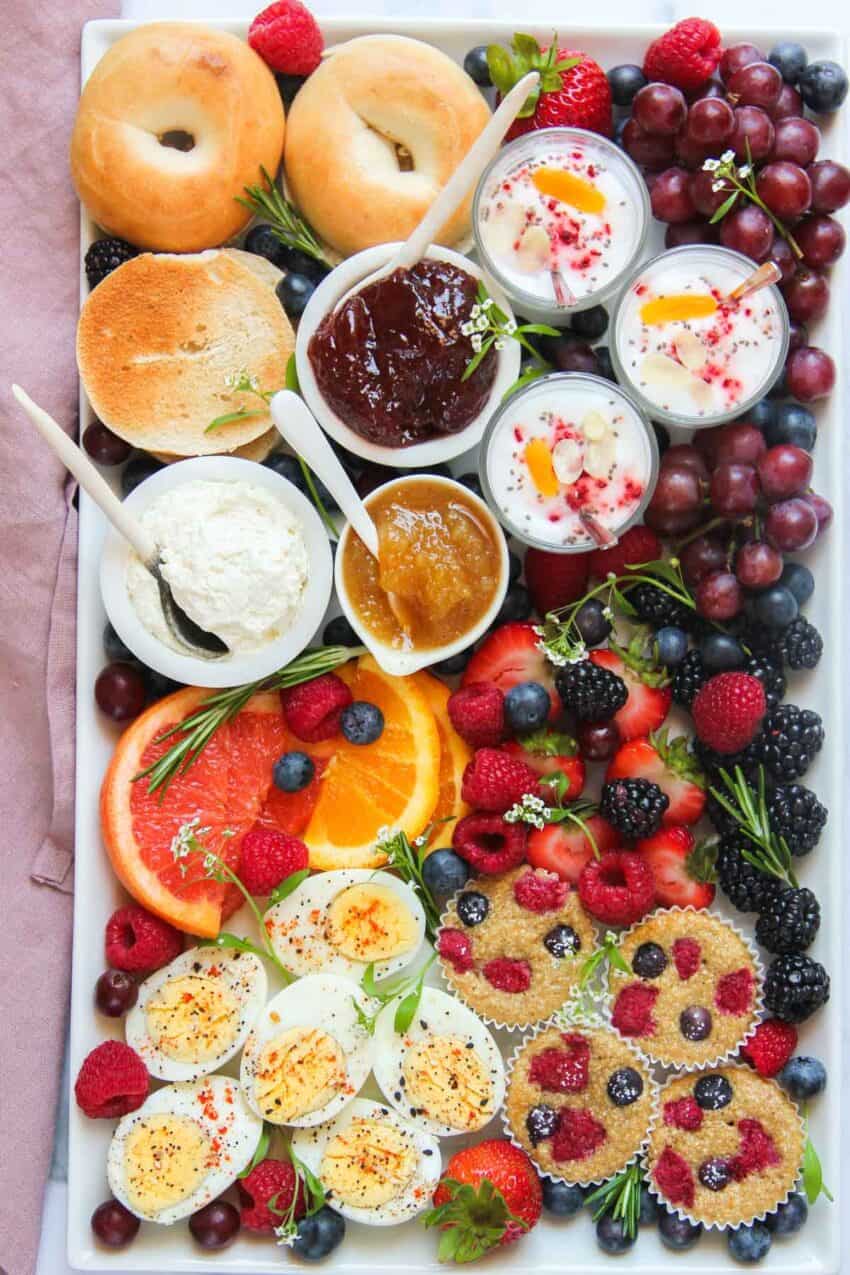 Breakfast Charcuterie Board with bagels, spreads, yogurt parfaits, mini muffins, eggs and fruits