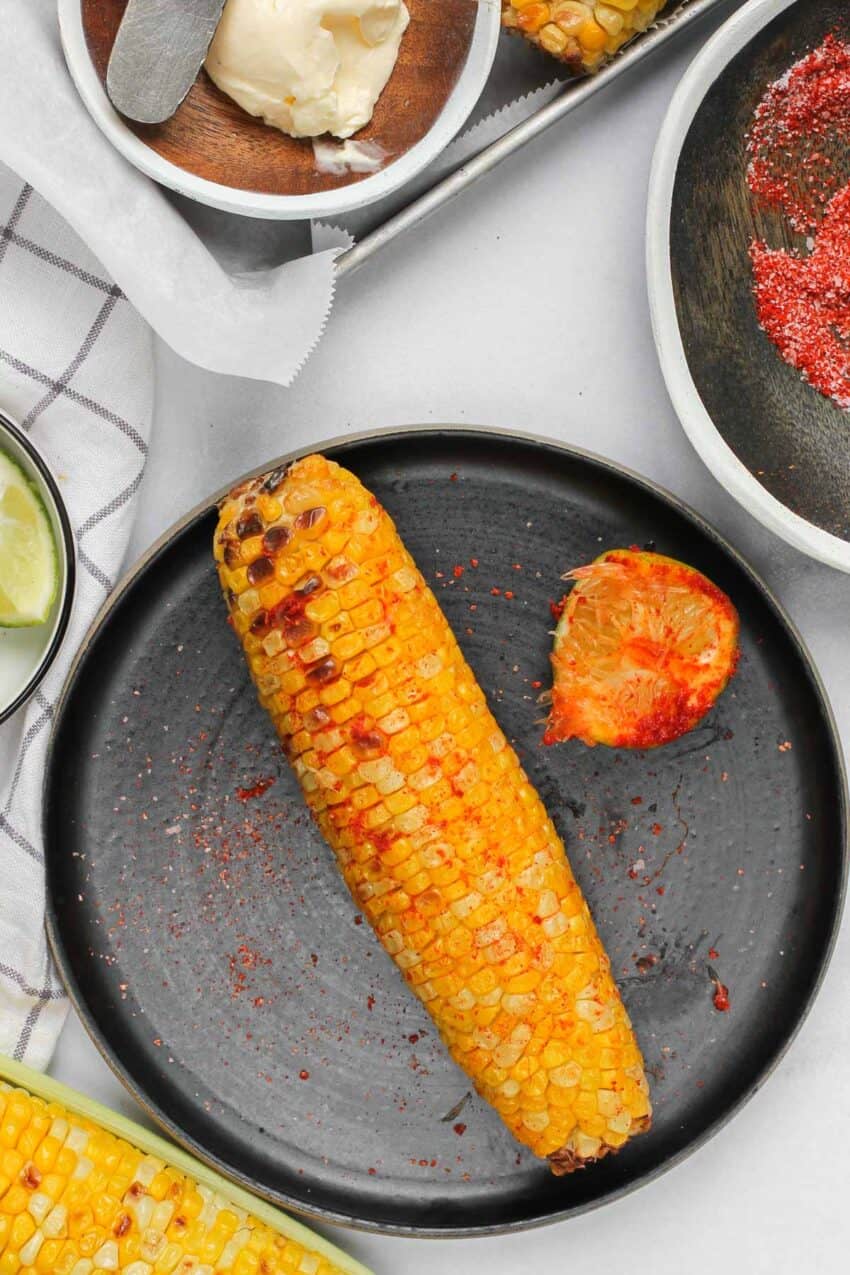 corn on the cob rubbed with salt, chili and lime on a black plate 