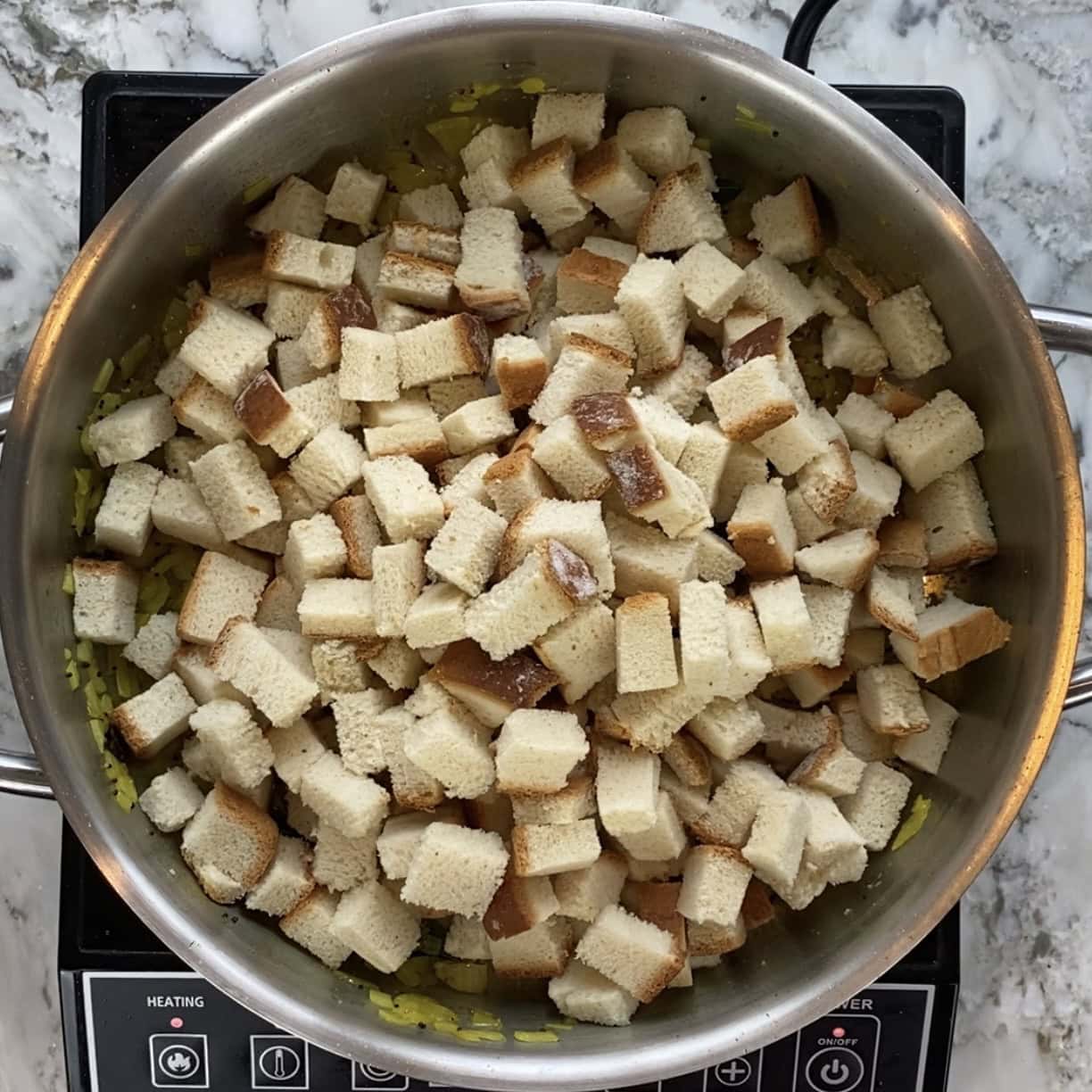 cubed bread added to stainless steel pan.