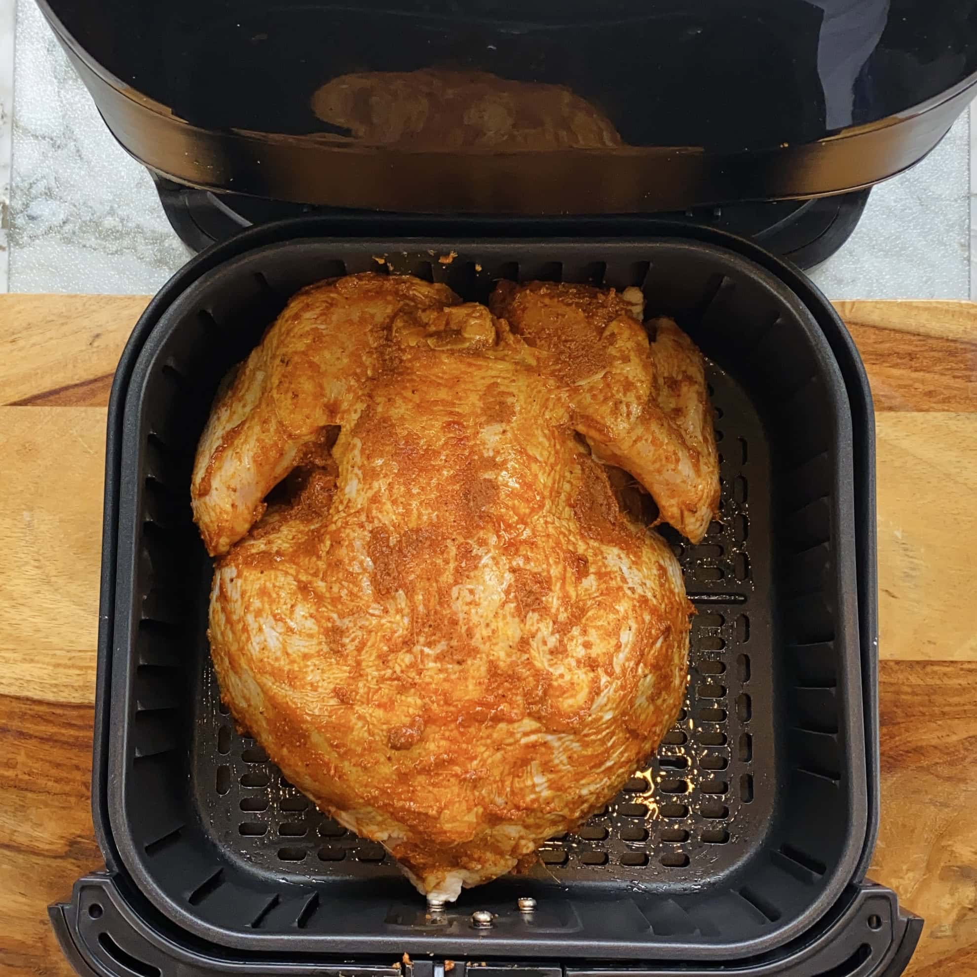 whole marinated chicken in air fryer basket.