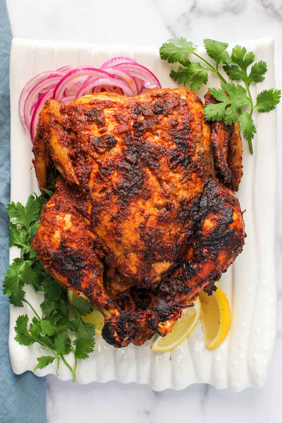 whole tandoori chicken in a platter with lemon wedges and sliced onions 