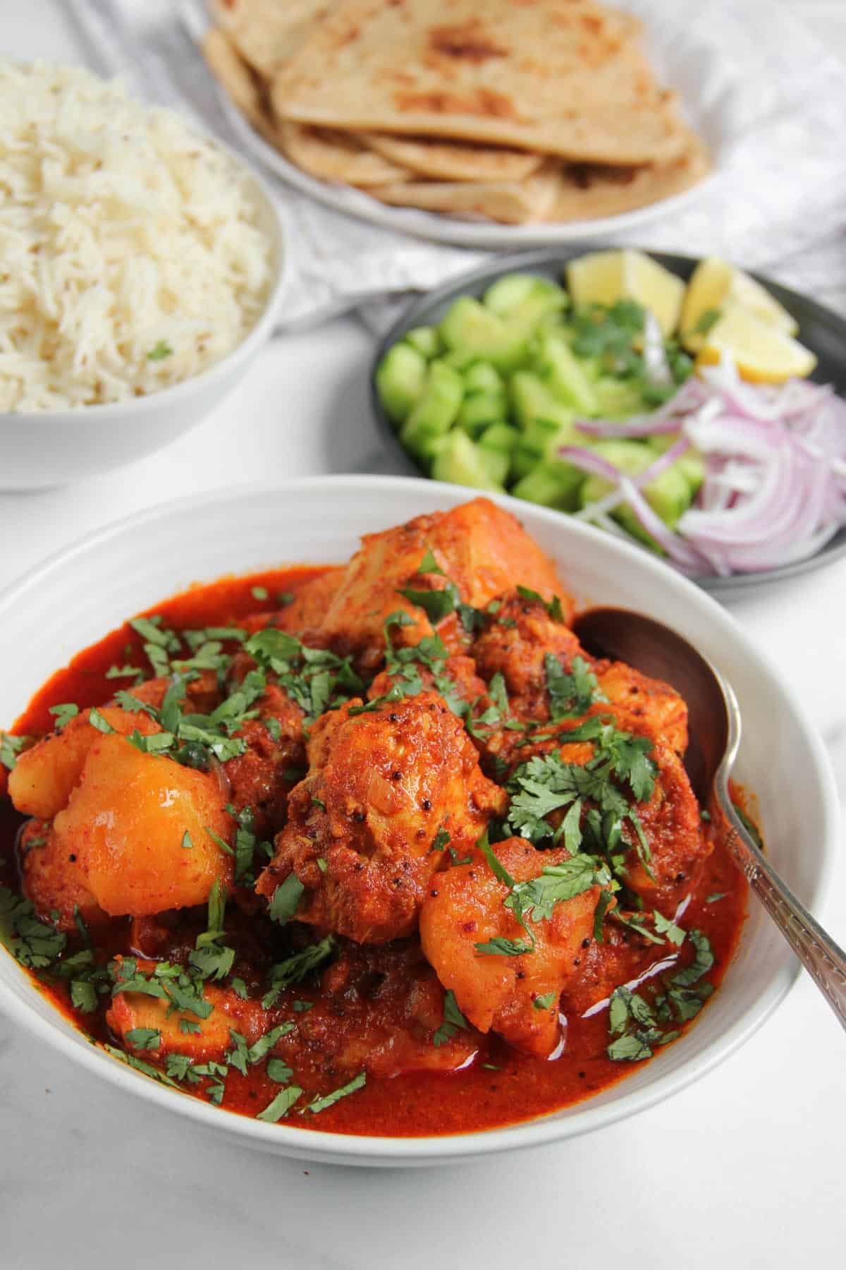Vindaloo  curry in a white bowl served with ice and parathas 