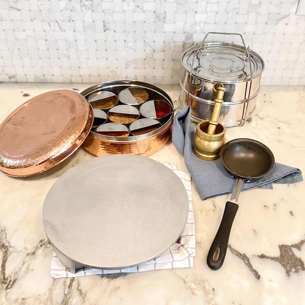 Spice box, stainless steel pots, mortar pestle and rolling chakla on kitchen counter 