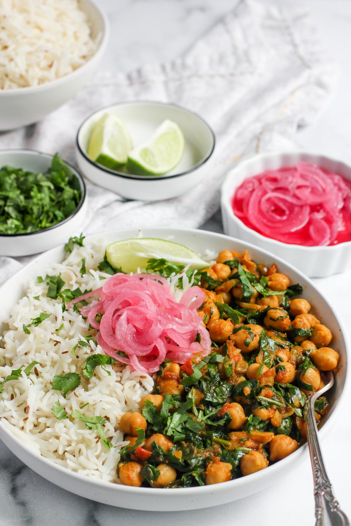 chana saag served in a white bowl with rice, pickled onions and lime wedge