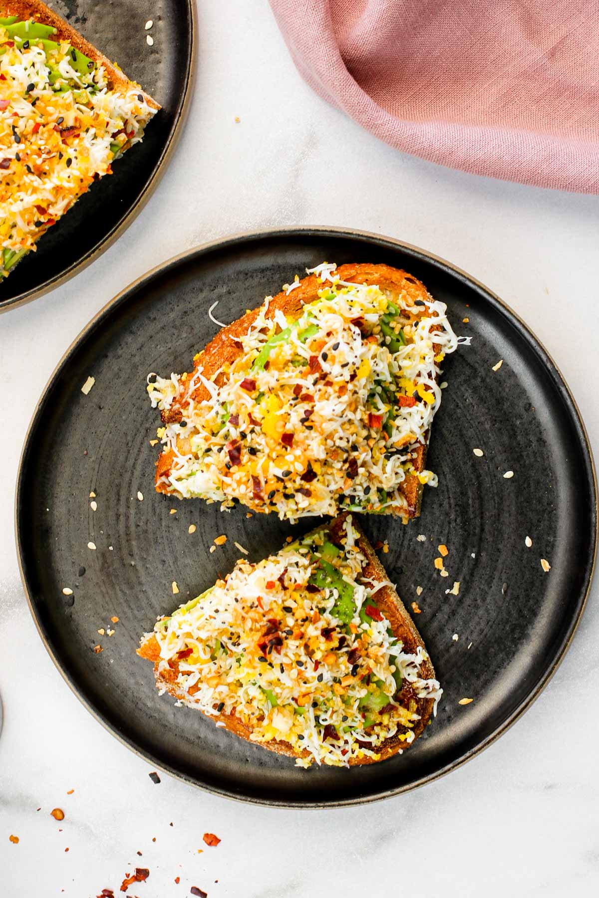 avocado toast with grated egg, everything bagel seasoning and chili flakes served on black plates