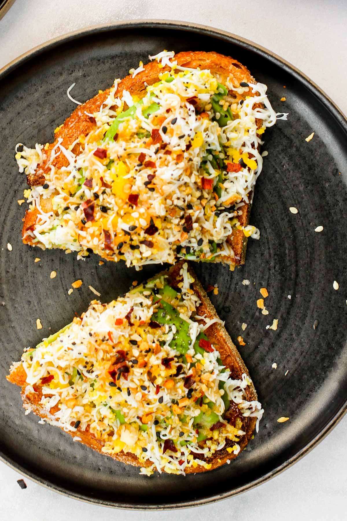 avocado toast with grated egg, everything bagel seasoning and chili flakes served on a black plate