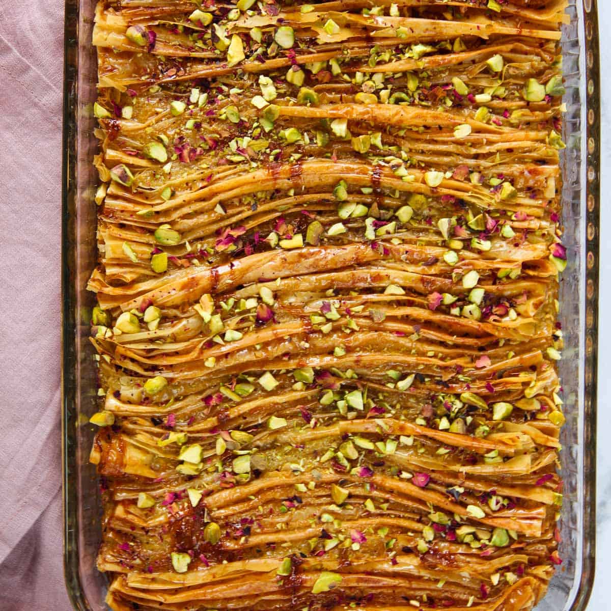 Phyllo dough crinkle cake garnished with pistachios and rose petals in a glass pan