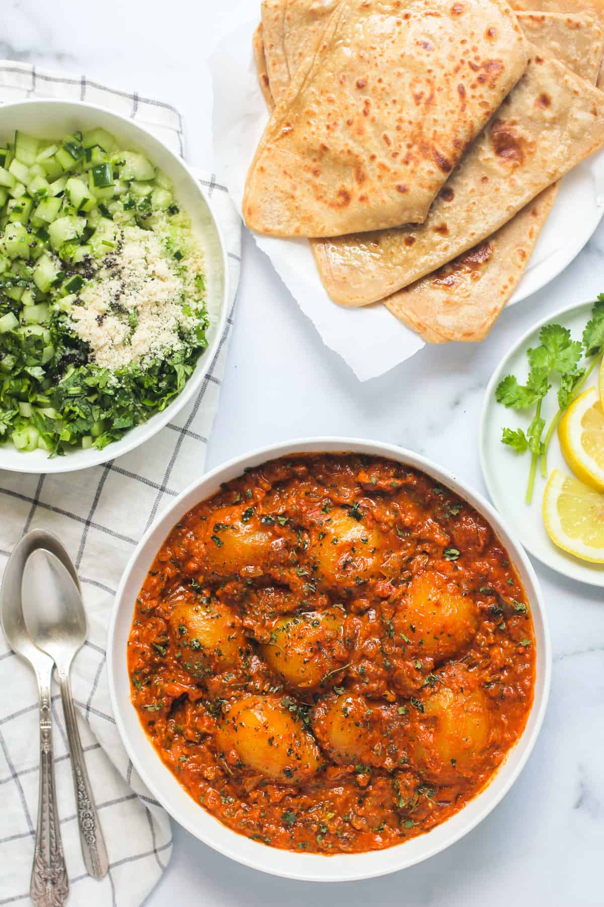 Curried potatoes served in a white bowl with parathas and salad on the side 