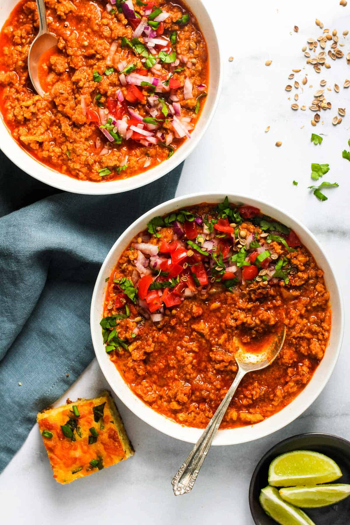 Ground chicken chili served in two white bowls garnished with onion, tomatoes and cilantro