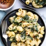 Spinach Artichoke Mac and Cheese served in a black plate with red chili flakes on the side