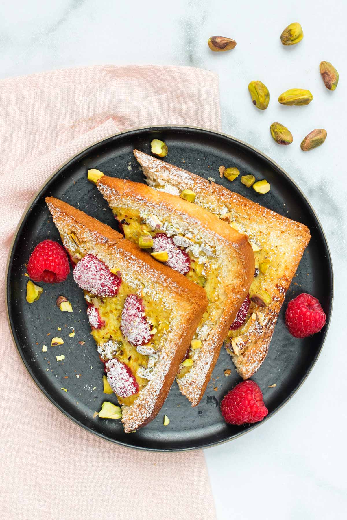 yogurt toast with berries and pistachios sprinkled with powdered sugar on a black plate