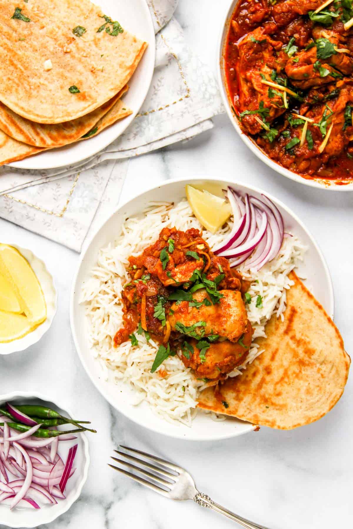 Chicken Karahi served over rice with naan in a white bowl 