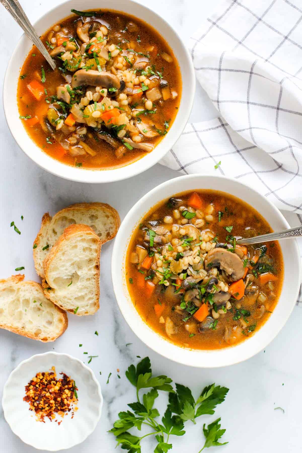 mushroom barley soup served in 2 white bowls with sliced baguette