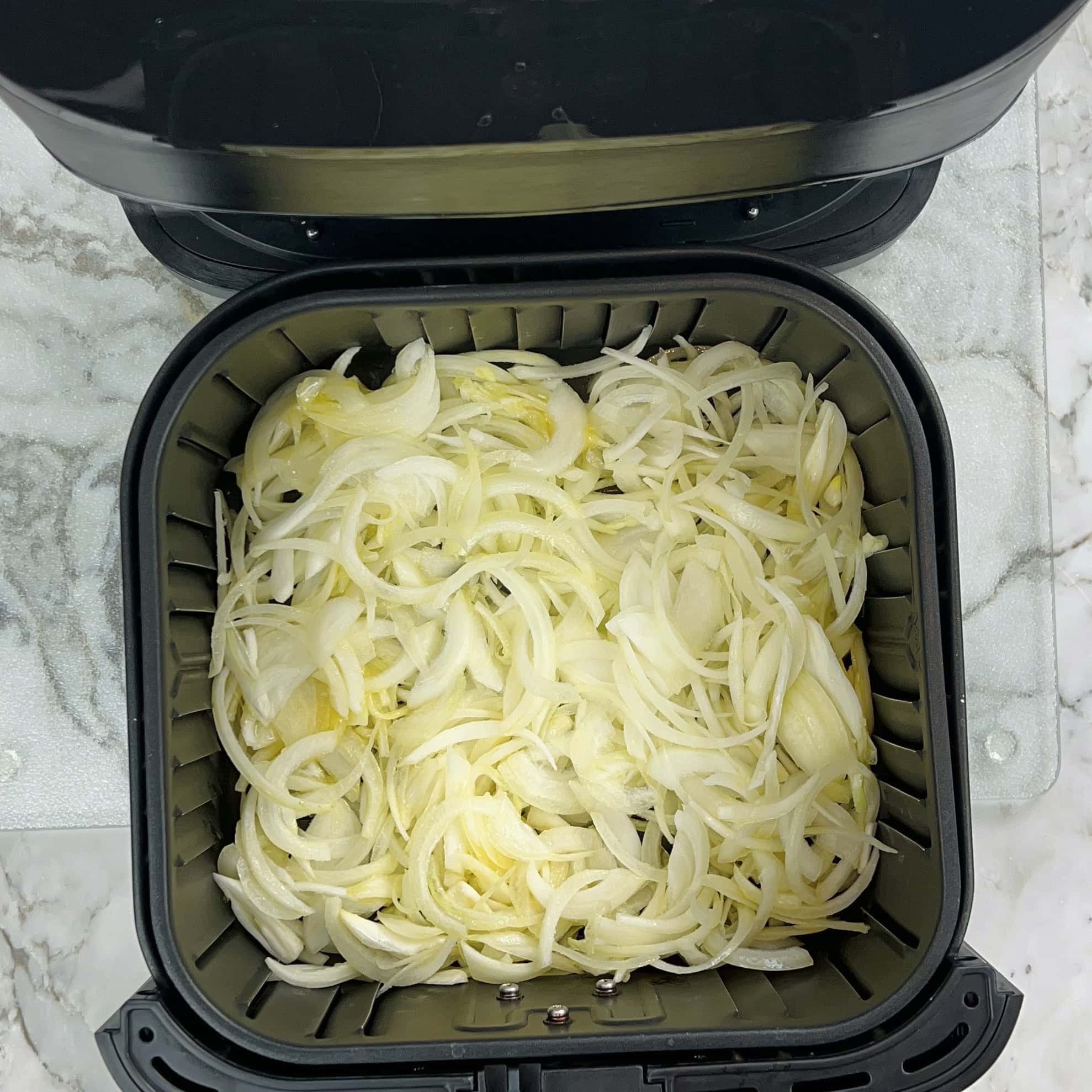 sliced onions in an air fryer basket.