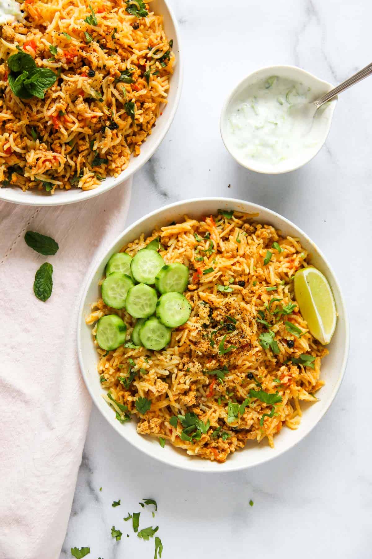 keema pulao served in two white bowls with raita