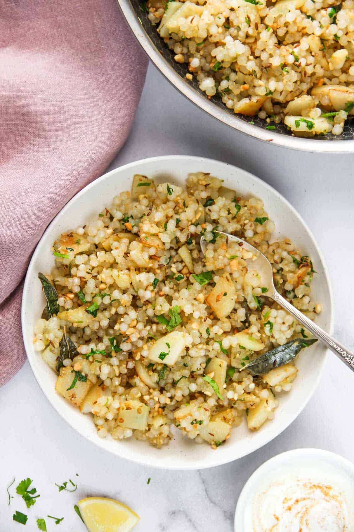 Sabudana khichdi in white bowl with lemon wedge and yogurt
