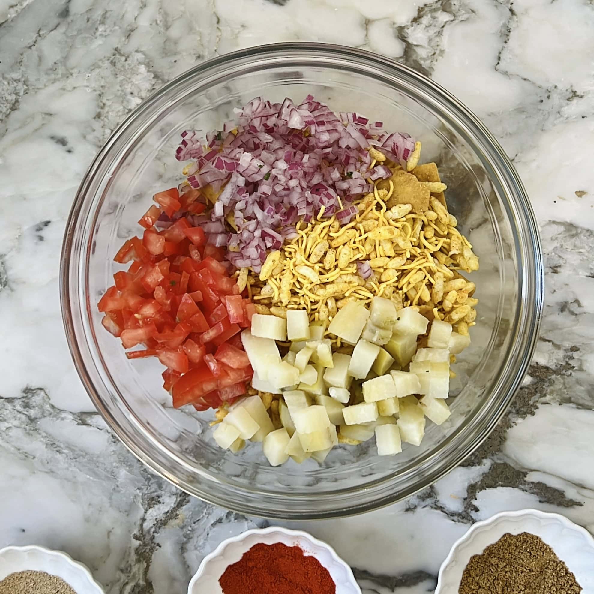 bhel topped with diced onions, potatoes and tomatoes.