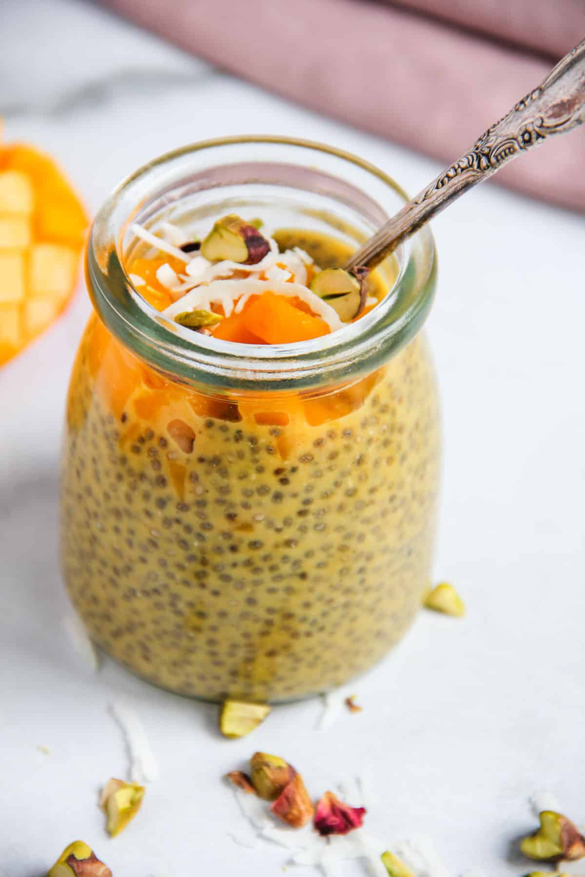 Mango chia pudding in a glass jar topped with diced mango, coconut and pistachios