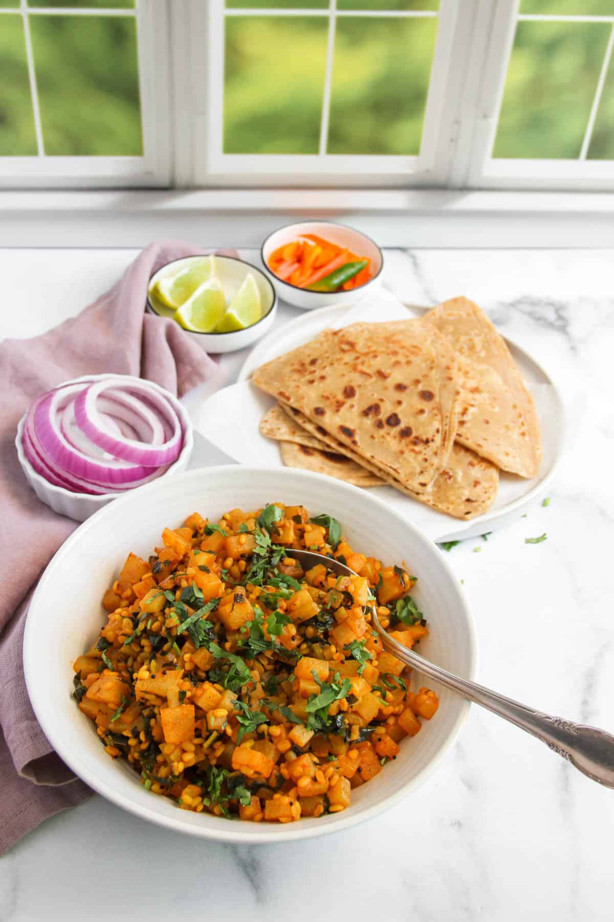 Kohlrabi curry served in a white bowl with parathas, onions, lime wedges and turmeric pickle 