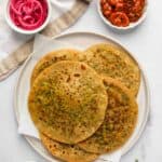 Palak Paneer parathas in a platter with small bowls of pickles on the side