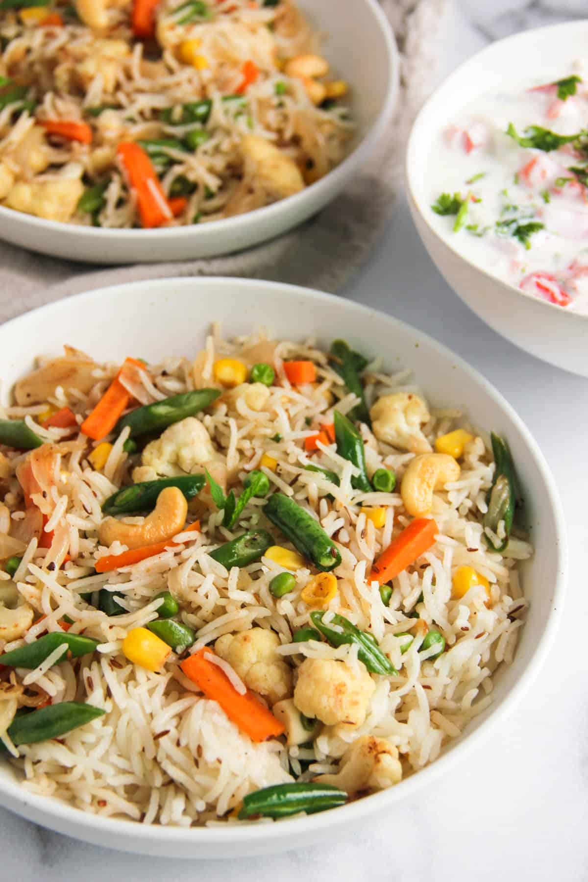 veg pulao in white serving bowls with raita on the side