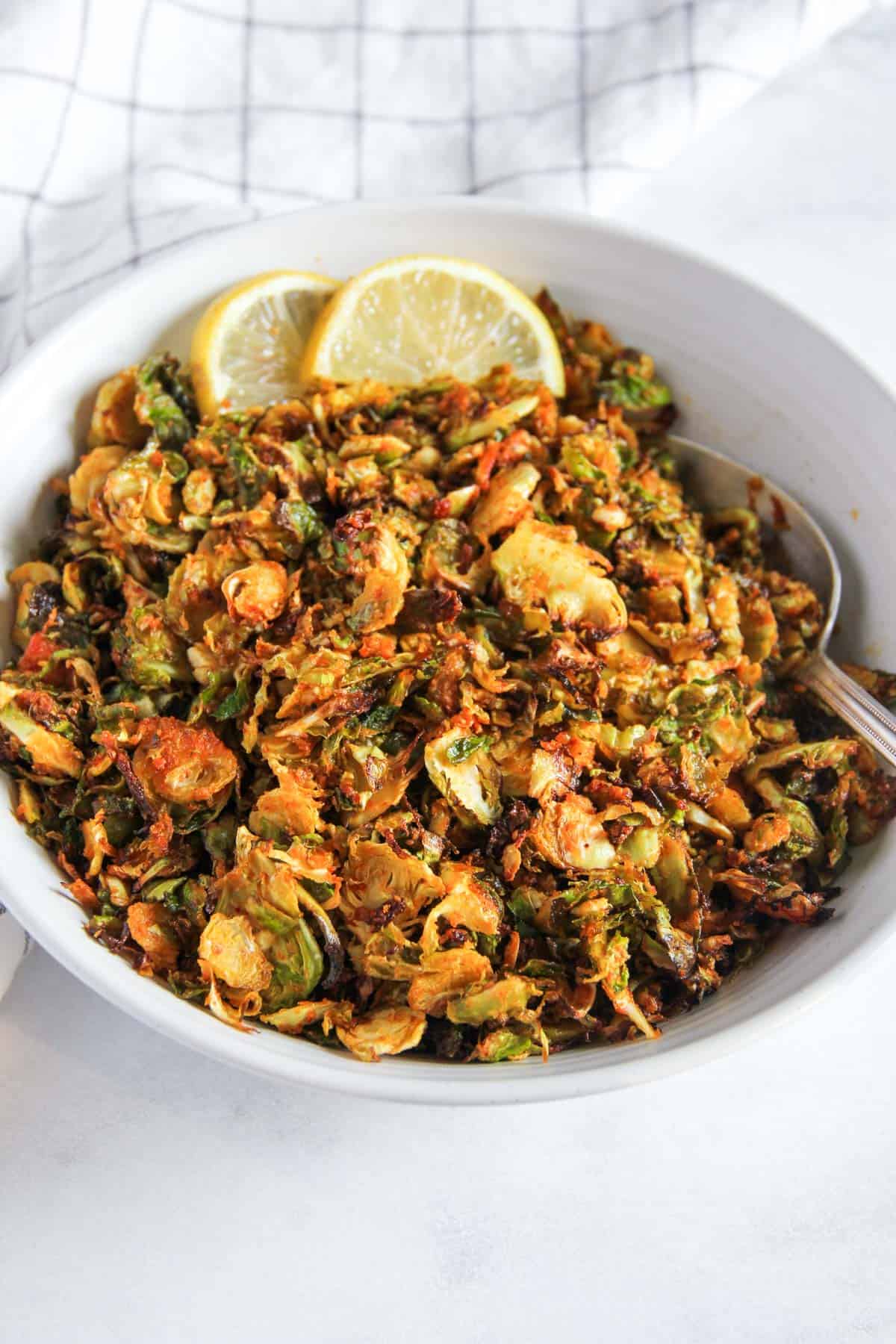 Crispy shaved Brussels sprouts in a white bowl with lemon wedges 