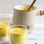 golden turmeric milk served in two glasses with a pot in the background