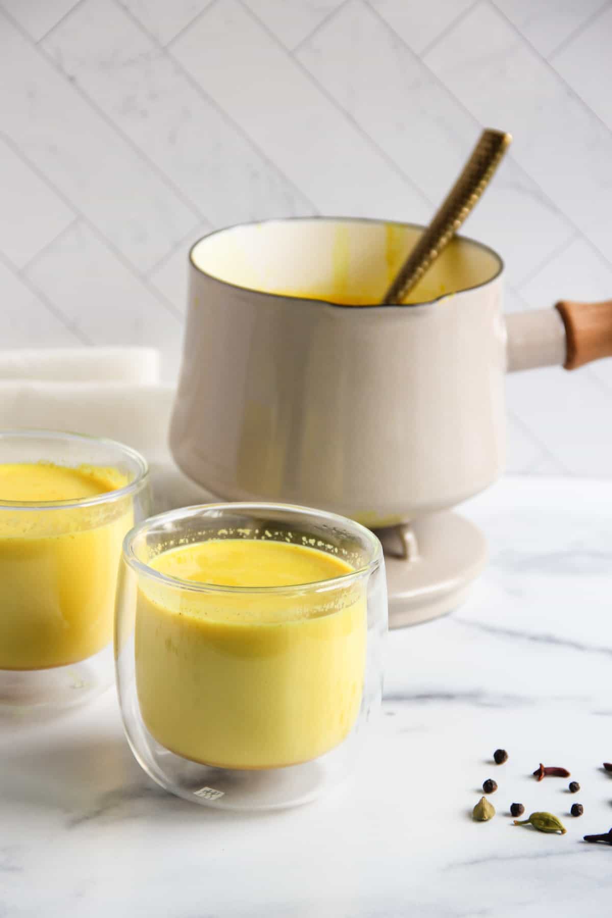 golden turmeric milk served in two glasses with a pot in the background
