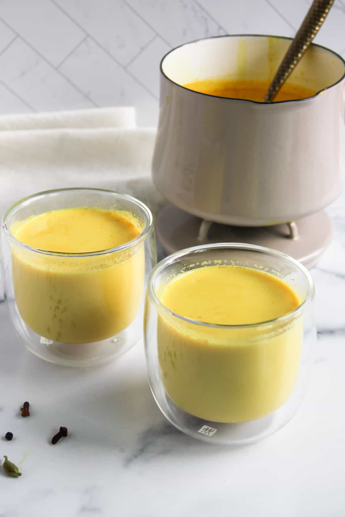 haldi doodh served in two glasses with a saucepan 