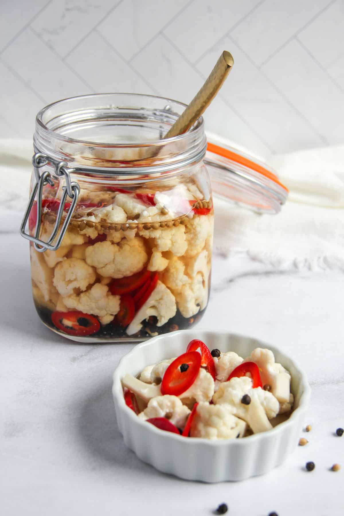 pickled cauliflower with red chilies and whole spices in a glass jar and small serving dish 
