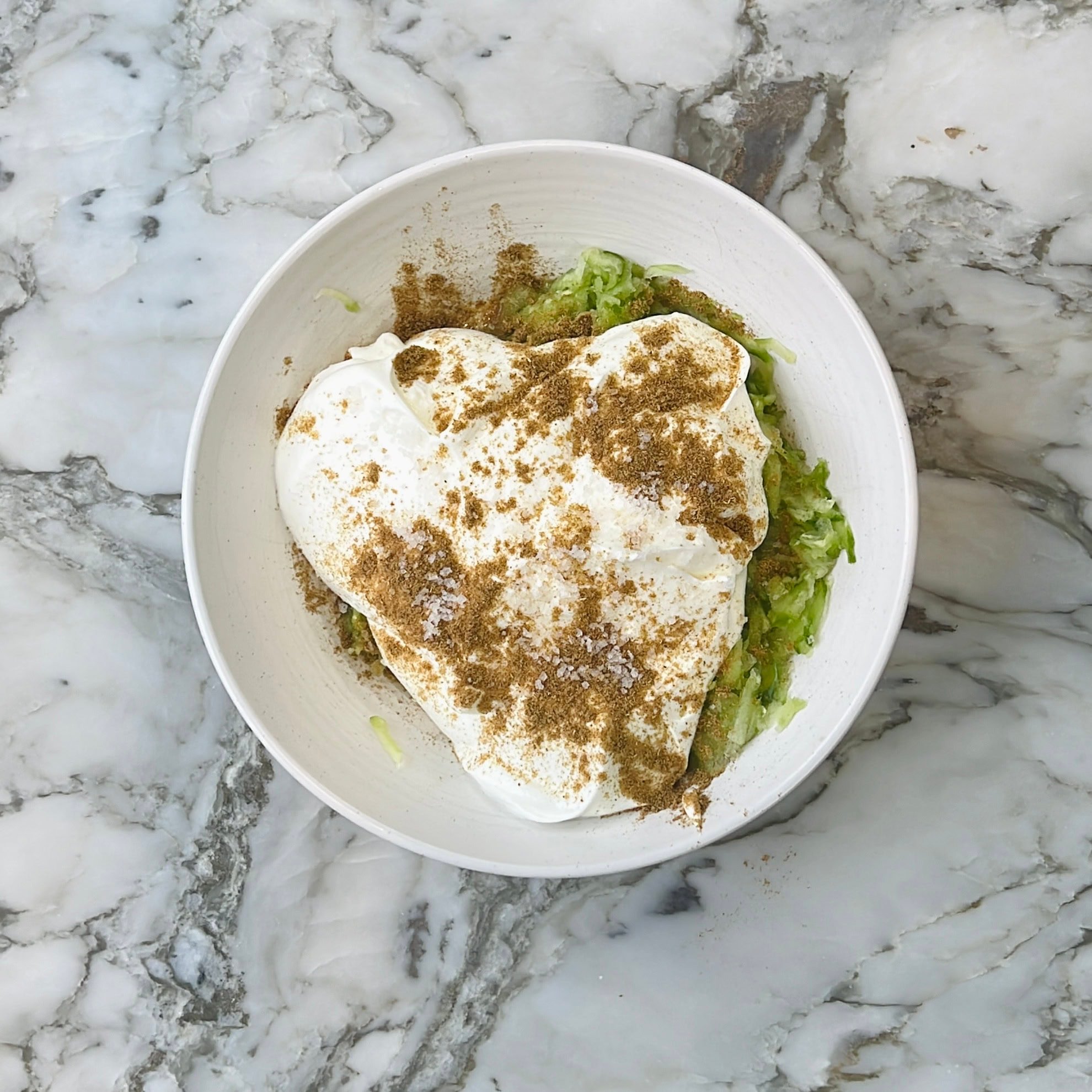 yogurt and cumin powder added to grated cucumbers
