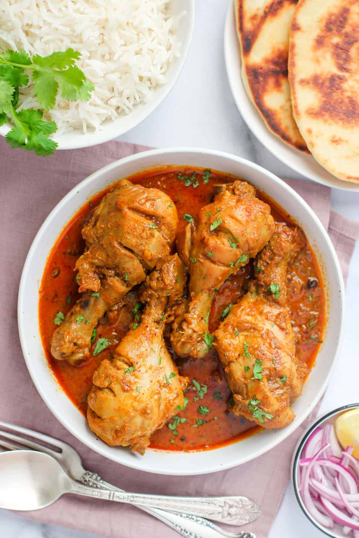chicken korma served in a white bowl with rice and naan on the side