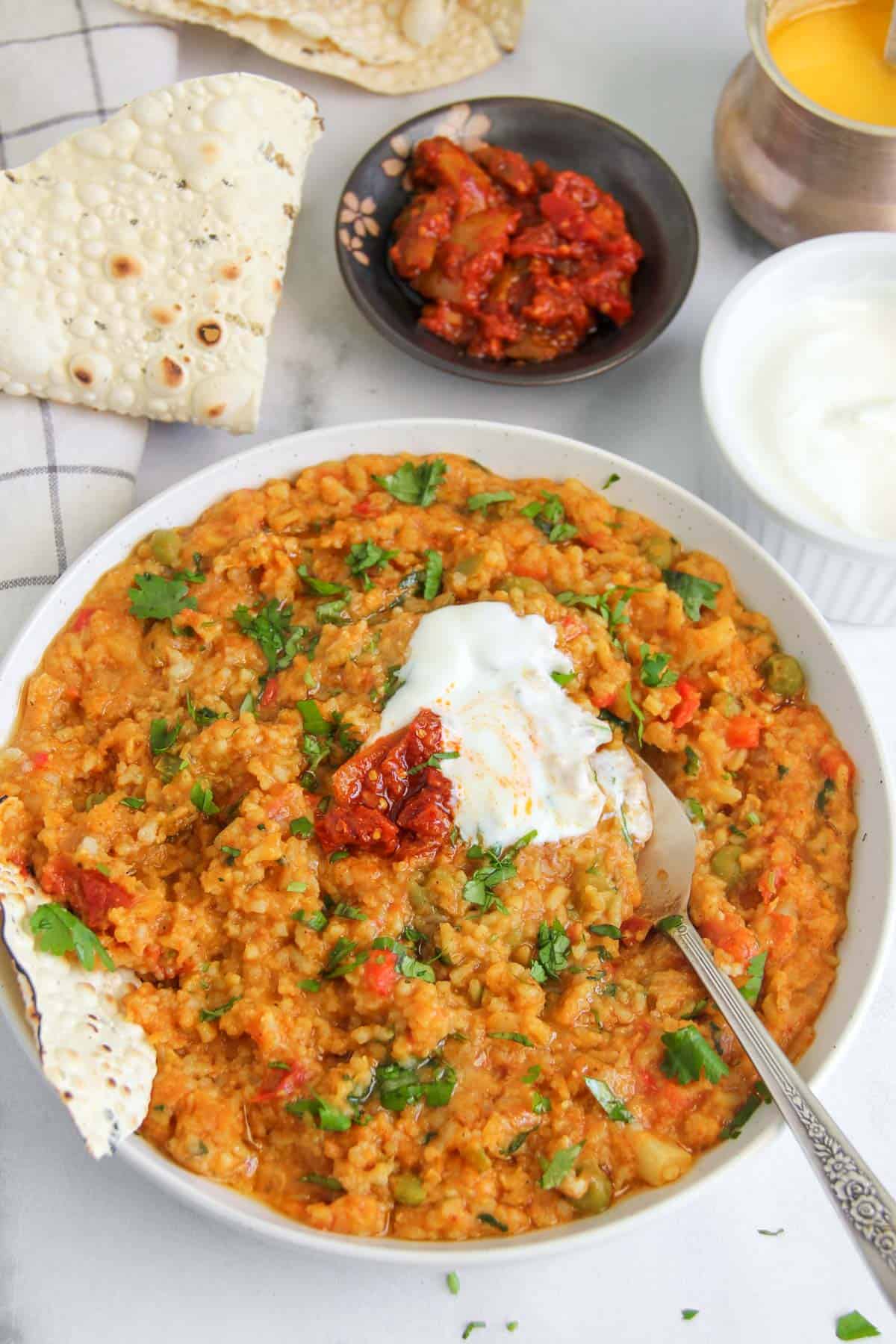 Khichdi served in a white bowl with yogurt and pickles 