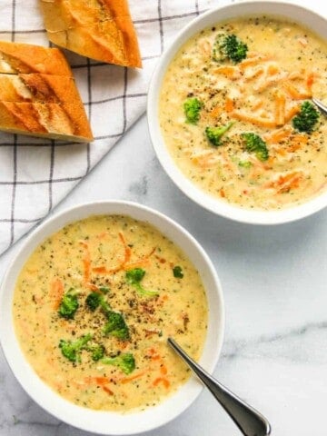 broccoli cheddar soup served in two white bowls with bread on the side