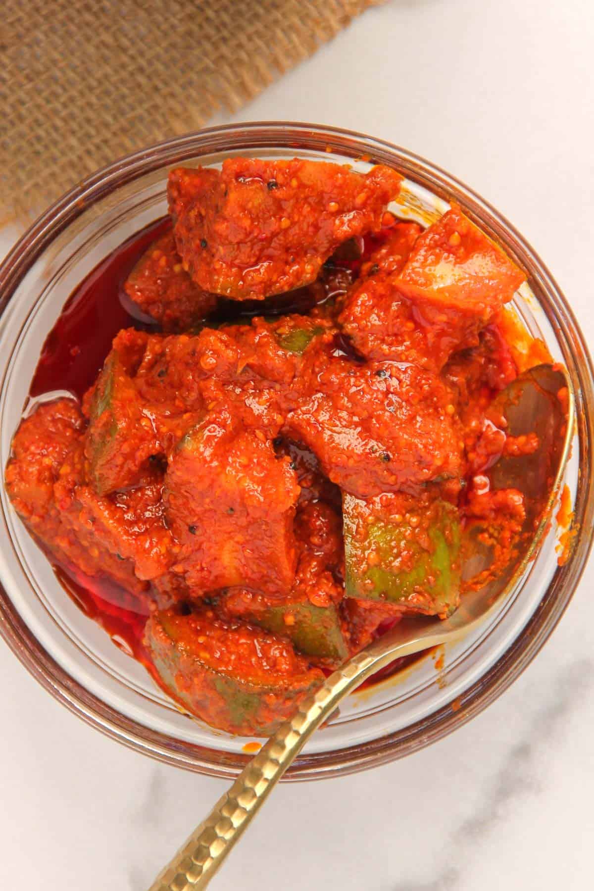 mango pickle in a glass serving bowl  with a spoon 