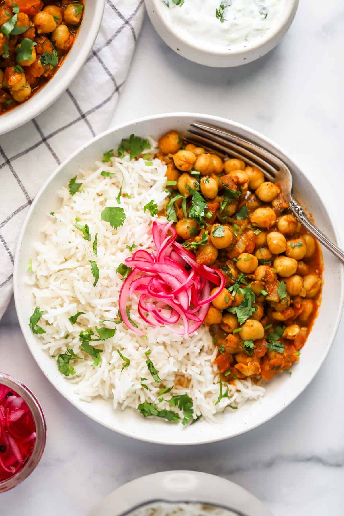Steamed rice and chana masala served in a white bowl with pickled onions 