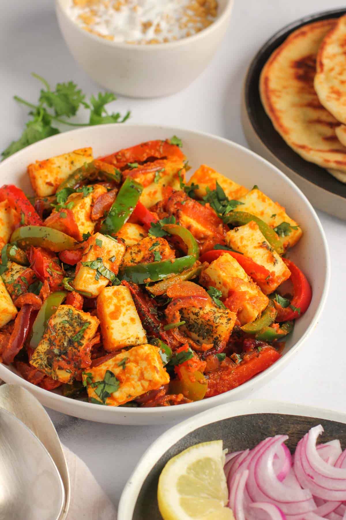 paneer jalfrezi alongside lemon wedges, onions, naan and raita