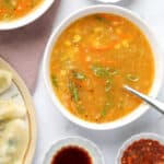 sweet corn soup served in white bowls with soy sauce and chili sauce on the side