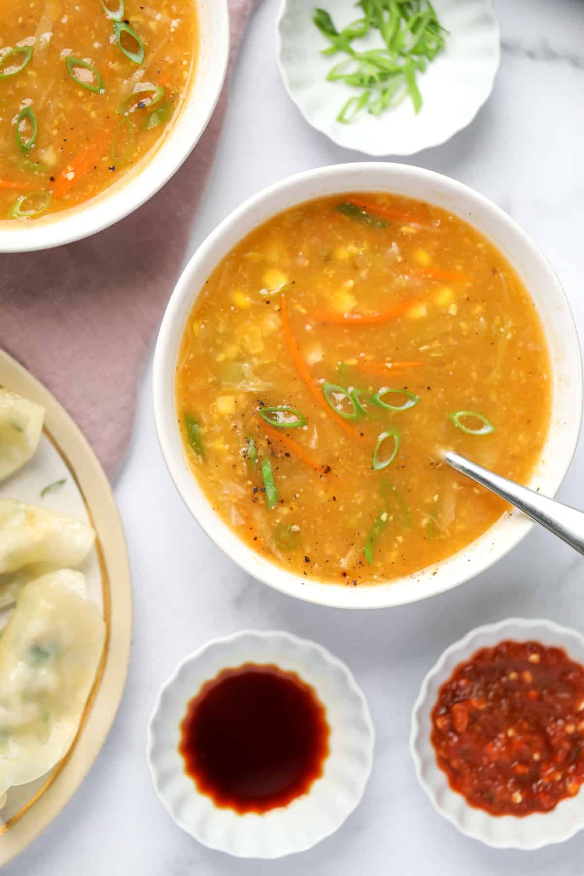 sweet corn soup served in a bowl with soy sauce and chili sauce on the side