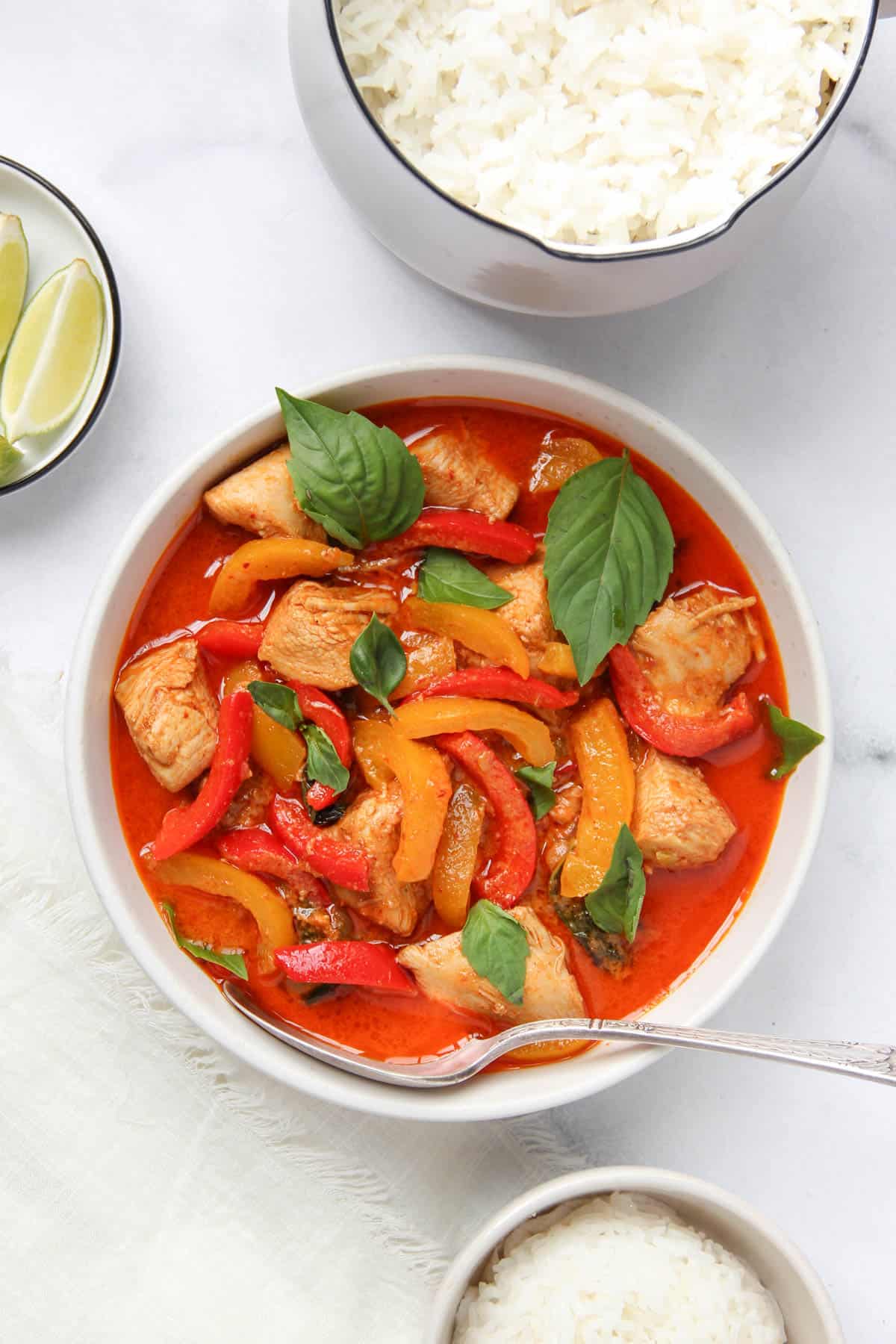 panang curry chicken served in a white bowl garnished with basil leaves with rice on the side 