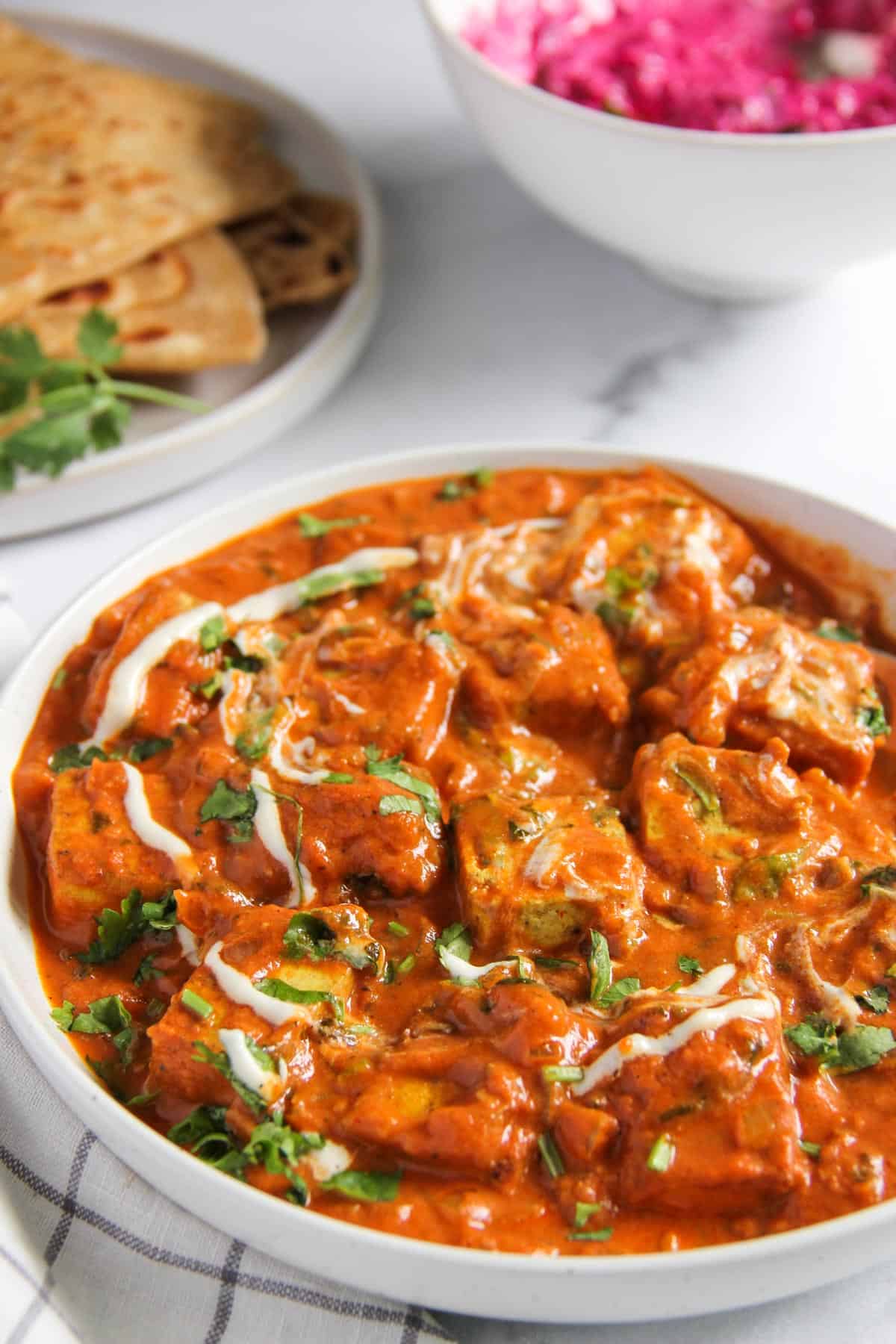 tofu makhani in a white bowl garnished with cream and cilantro 